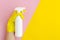 Hand with yellow glove holding a spay bottle closeup on bright split color background. Pink and yellow vibrant duotone