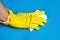 Hand in yellow protective glove with white melamine household sponge on blue background.