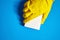 Hand in yellow protective glove with white melamine household sponge on blue background. Means for cleaning surfaces