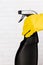 Hand in yellow rubber glove holding black plastic spray detergent bottle. Household chemicals. Cleaning product