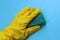 Hand in yellow rubber glove holding a sponge for washing