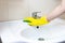 Hand in yellow rubber glove washes bathroom sink with a sponge. Clean up concept