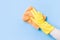 Hand in a yellow rubber glove washes the wall with an orange soft rag, cleaning and washing the walls, blue background copy space