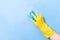 a hand in a yellow rubber glove washes a wall with a wet foamy blue sponge, foam blue background copy space