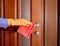 Hand in a yellow rubber glove wipes the door knob with a red rag. disinfect ingesited at home from bacteria and viruses