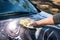 Hand with yellow sponge and soap are washing the car