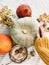 Hand in yellow sweater holding pumpkin and nuts, yellow flowers, fall leaves on rustic table, flat lay. Fall decor and arrangement