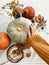 Hand in yellow sweater holding pumpkin and nuts, yellow flowers, fall leaves on rustic table, flat lay. Fall decor and arrangement