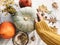 Hand in yellow sweater holding pumpkin and nuts, yellow flowers, fall leaves on rustic table, flat lay. Fall decor and arrangement