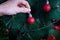 The hand of a young caucasian woman hangs a red ball on the Christmas tree. New Year preparation concept