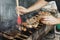 Hand of young man lubricates the meat with a sauce brush on long rectangular barbecue with smoke on the street outdoor.