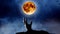 Hand of a zombie comes out of the ground from behind bats and yellow moon. Night sky background