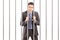 Handcuffed businessman in suit posing in jail and holding bars