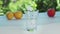 Handful of ice cubes throwing in empty glass, close shot. Yellow lemons, red apple and glass on white surface. Green