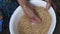 Handful of old woman mixes raw buckwheat grains in white bowl