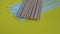Handheld closeup shot of lots of plastic drinking straws on a colourfull yellow background - a hand of a person put a