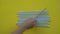 Handheld closeup shot of lots of plastic drinking straws on a colourfull yellow background - a hand of a person put one