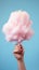 Handheld Delight: Whimsical Pink Cotton Candy Against a Serene Blue Sky. Generative AI