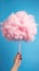 Handheld Delight: Whimsical Pink Cotton Candy Against a Serene Blue Sky. Generative AI