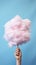 Handheld Delight: Whimsical Pink Cotton Candy Against a Serene Blue Sky. Generative AI