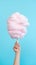 Handheld Delight: Whimsical Pink Cotton Candy Against a Serene Blue Sky. Generative AI