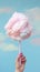 Handheld Delight: Whimsical Pink Cotton Candy Against a Serene Blue Sky. Generative AI