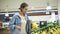 Handheld footage of pretty young girl in shirt selecting fruits in supermarket. Puts some banans into cellophane bag