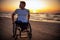 Handicapped man in wheelchair and his girlfriend alone on a beach at sunset