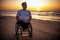 Handicapped man in wheelchair and his girlfriend alone on a beach at sunset