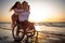 Handicapped man in wheelchair and his girlfriend on a beach at sunset