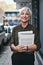 Handling business in the vibrant streets. Portrait of a cheerful mature businesswoman carrying books and paperwork while