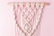 A handmade 100% cotton macrame wall decoration hanging on pink wall. Decoration for the interior. Trendy handcrafted decor for