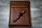 Handmade brown leather laptop case on a wooden table with a black clock. Flatlay.