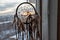 Handmade dreamcatcher hanging by the window in sunrise twilight. Urban city landscape on dackground. Black silhouette of