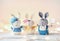 Handmade knitted rabbits. 3 Easter bunnies in a row on light background. Bunny girl, sailor and a scientist