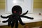 Handmade knitted toy black octopus in the interior of a beautiful bright room lies on a white shelf. Hobby