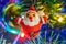 Handmade Santa Claus cloth figure on the branch of christmas fir against luminous colored garland and decorative balls close-up