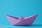 Handmade violet paper boat on light blue background. Origami art