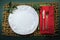 Handmade white plate with red and green napkins with holly on a rustic woven mat casual Christmas background