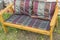 A handmade wooden chair covered with a textile blanket and Burgundy pillows stands on the grass in the garden on a Sunny summer