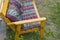 A handmade wooden chair covered with a textile blanket and Burgundy pillows stands on the grass in the garden on a Sunny summer