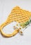 Handmade yellow macrame bag with bouquet of chamomile on the linen background