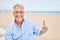 Handosme hispanic man with grey hair smiling happy at the beach, enjoying holidays pointing with finger at copy space