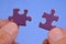 Hands assembling two puzzle pieces close up on blue background