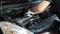 The hands of an auto mechanic use a socket wrench to unscrew parts under the hood of a car.