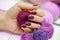 Hands with a beautiful solid purple manicure. A woman holds a ball of knitting thread.