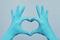Hands in blue doctor gloves making heart on gray background. Medical assistance concept