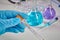 Hands in blue gloves holding Coronavirus testing kit. Medical flasks, colorful chemical reagents. Ampoules, syringe