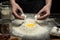 Hands are breaking an egg into flour to make dough