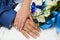 Hands of bride and groom with golden wedding rings and blue and white wedding bouquet